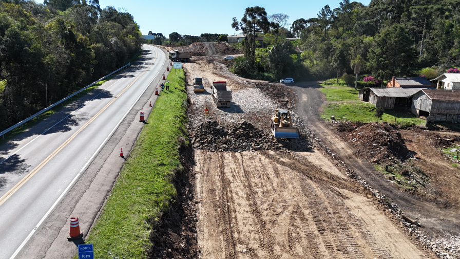 Perspectiva aérea de uma rodovia, com obras na marginal e maquinários trabalhando.