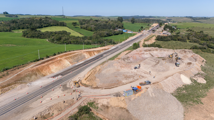 vista aerea da construção de uma rodovia, com maquinário trabalhando e pessoas uniformizadas.