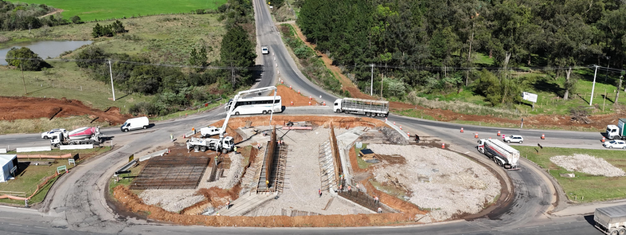 Vista aérea de uma rodovia com múltiplas faixas de tráfego próximas a edifícios, e plantações.