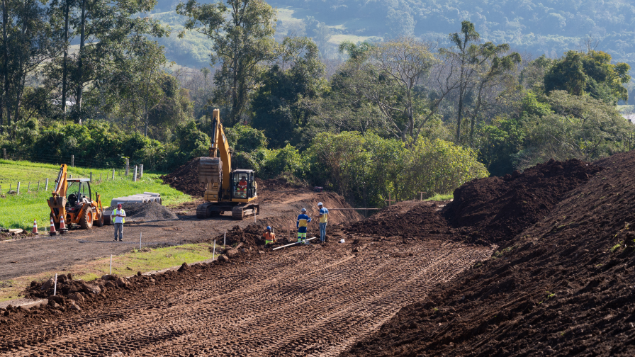Construção de uma rodovia, com maquinário trabalhando e pessoas uniformizadas.
