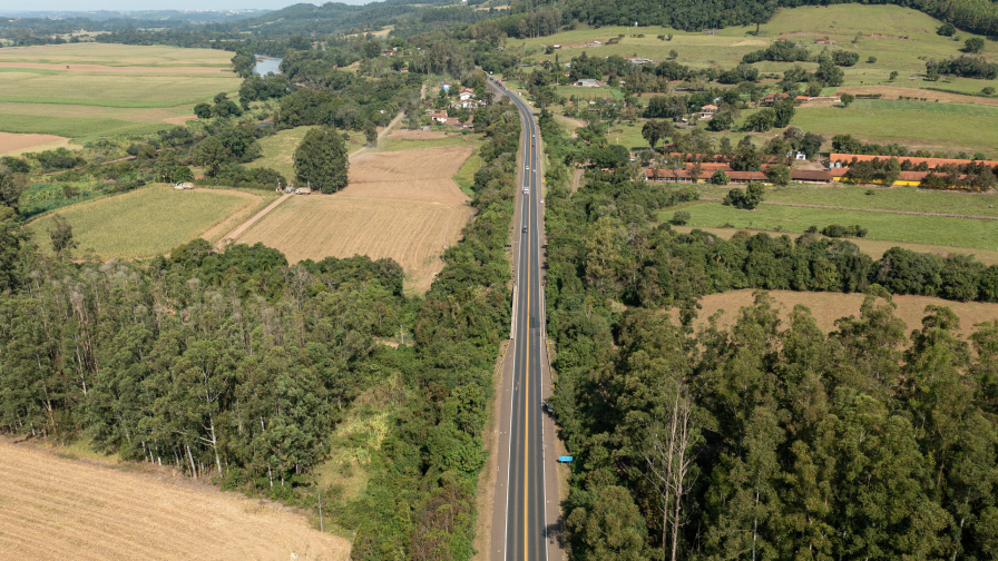 Perspectiva aérea de uma rodoviavia em meio à floresta, com construções as margens da rodovia.