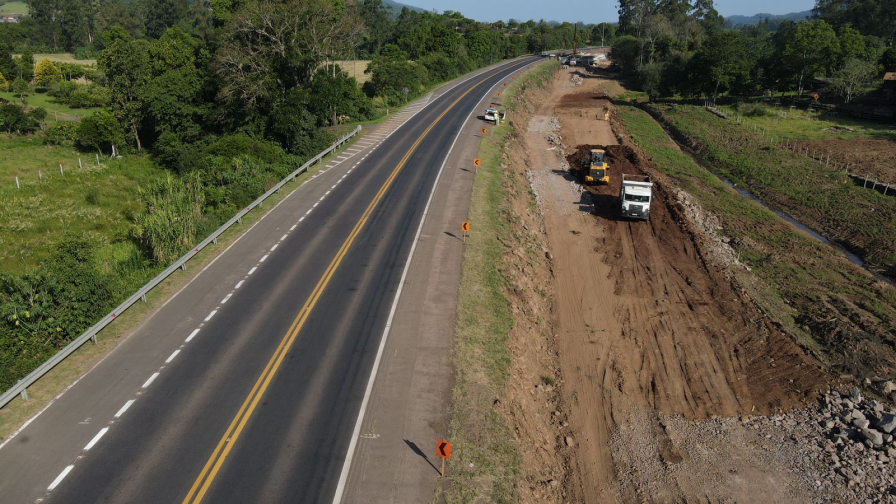 Perspectiva aérea de uma rodovia, com obras na marginal e maquinários trabalhando.