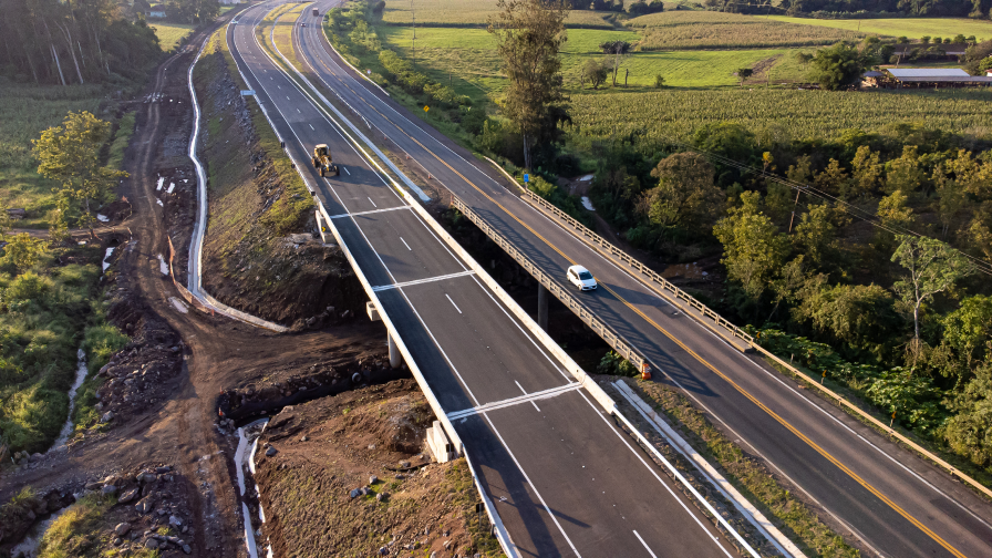 Perspectiva aérea de uma rodovia, com obras na marginal e maquinários trabalhando.