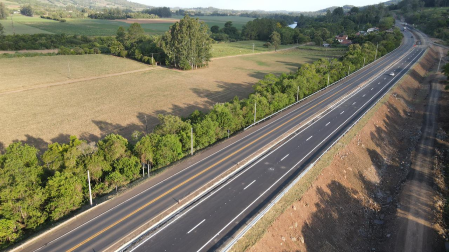 Perspectiva aérea de uma rodoviavia em meio à floresta, com construções as margens da rodovia.