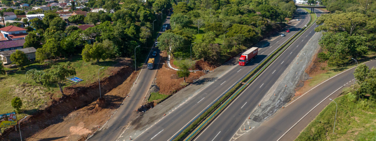 Vista aérea de uma rodovia com múltiplas faixas de tráfego próximas a edifícios, e plantações.